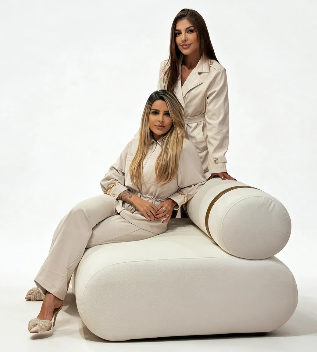 Larissa e Vanessa Amorim em estúdio, vestindo tons de areia, sentadas em um pufe branco