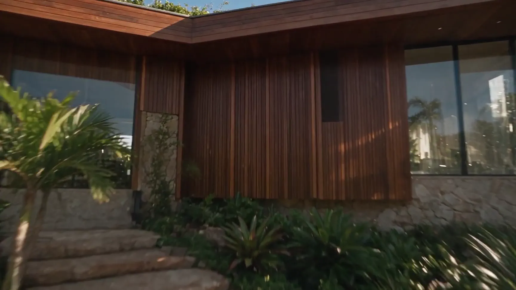 Entrada de uma casa contemporânea com fachada de madeira, escadaria de pedra e jardim tropical